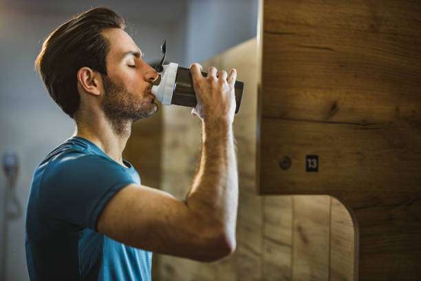 Thirsty athletic man drinking refreshing drink in a gym's dressing room